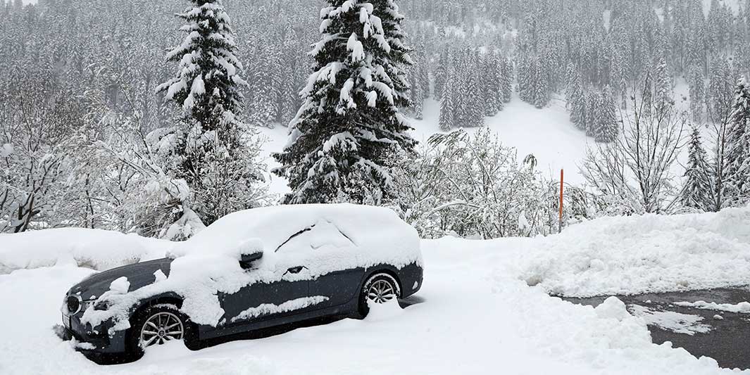 Ein eingeschneites Auto steht am Sonntag in Südbayern am Riedbergpass in winterlicher Landschaft.