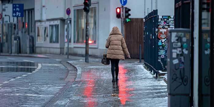 Eine Fußgängerin passiert einen Gehweg, der sich nach Blitzeis in eine Rutschbahn verwandelt hat. Eisregen hat für spiegelglatte Böden gesorgt.