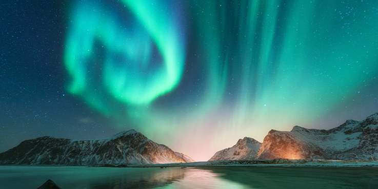 Foto mit Bergen, Wasser, dunklem Himmel und leuchtenden Polarlichtern.